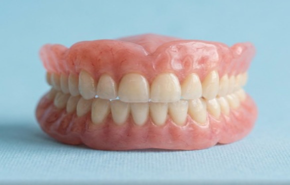 A close-up of a complete set of realistic, custom-made upper and lower dentures resting on a light blue clinical surface.